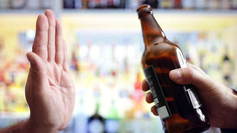 een hand en een flesje bier waarbij de hand zegt geen alcohol drinken